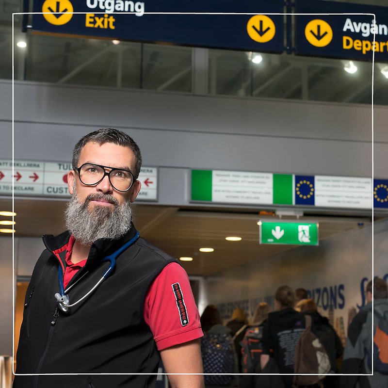 Närbild på en manlig Distriktsveterinär med långt grått skägg och glasögon som står inne på en flygplats. Han arbetar som gränskontrollant.